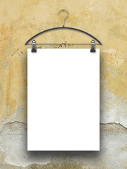 Close-up of one hanged paper sheet with clothes hanger on cracked beige plaster wall background