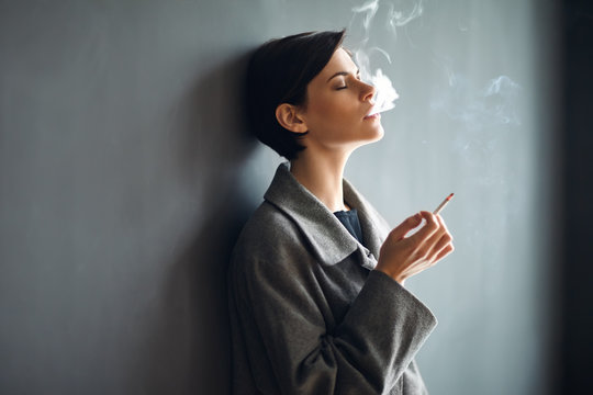 Portrait of fashionable woman smoking a cigarette on dark backgr