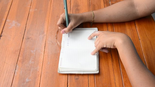 Thai woman write note book on wooden table