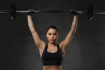 young woman flexing muscles with barbell in gym