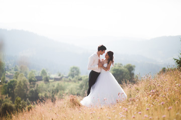 Romantic fairytale couple newlyweds posing at sunset on a background of mountains