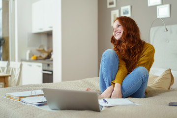glückliche junge frau sitzt auf dem bett mit laptop und unterlagen