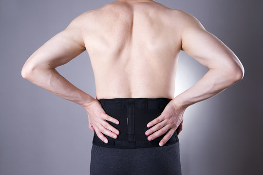 Man with a medical belt for the back on a gray background