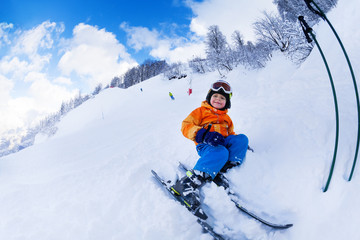 Little skier boy sit with ski in snow resting