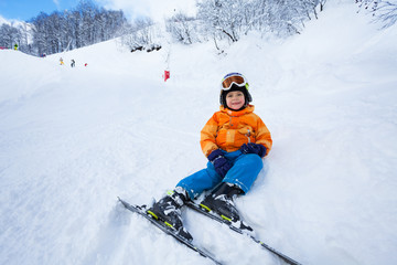 Little boy rest after ski lesson sitting in snow