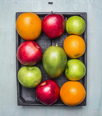 oranges, mangoes, apples of different varieties in a wooden box on wooden rustic background top view close up