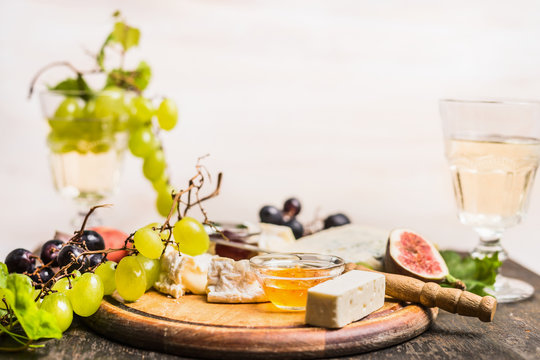 cheese plate with grapes, gorgonzola, camembert, a glass of wine, cheese knife on a cutting board on wooden rustic background  close up