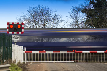 Close up of train speeding through English countryside crossing a level crossing