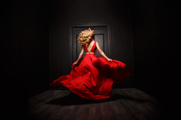 Elegant and sexy woman in the red evening fluttering dress is capture in move, running away from the ceremony (the
ball), the wooden door is on the background - 104190873