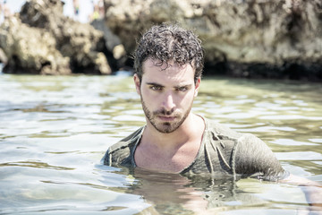 Athletic man in the sea or ocean by rocks, wet t-shirt