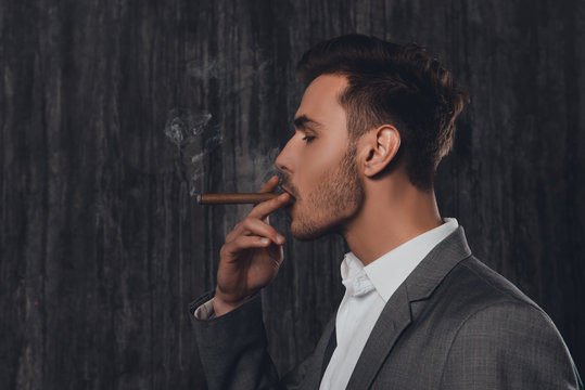 Side view portrait of handsome man in suit smoking a cigar