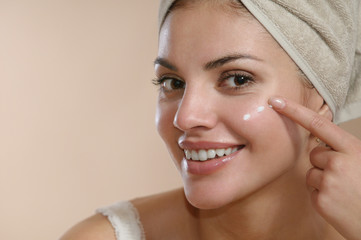 Beautiful young woman wrapped in towel spreading cream on her face