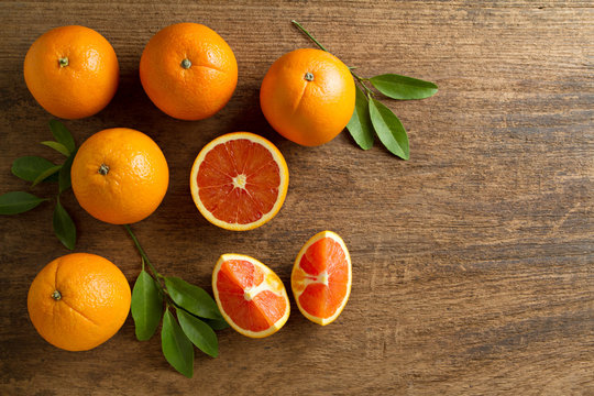 Fresh oranges with slices and leaves on wooden background.