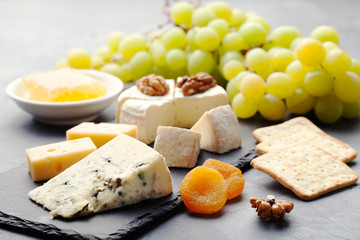Glass of white wine and assorted cheese with grape on a slate background Copy space