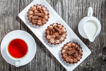 Chocolate cupcakes with a cup of tea and a jug of milk, top view