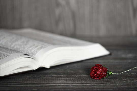 Black and white photo of an open book on a background of colored roses made of shiny beads. Focus on the rose