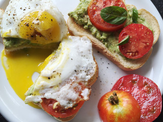 Runny egg on bread with mashed avocado, fresh tomatoes and black pepper 