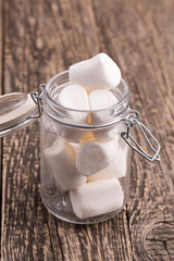Sweet marshmallows in a glass jar on wooden table.