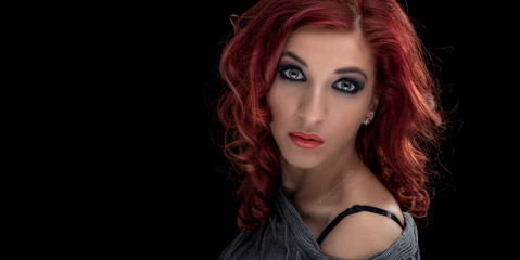 Beauty portrait of fashionable teenager girl with curly long red hair and perfect makeup shot against black background with copy space