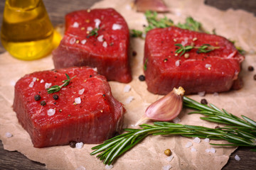 Raw beef steak with rosemary, thyme and garlic on wooden background