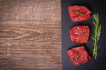 Raw beef steak with rosemary, thyme and garlic on wooden background