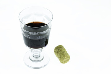 Classic embroidered wine glass half filled with red wine and a cork alongside isolated on white