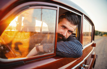 Fototapeta na wymiar brutal bearded man with a mustache in a shirt, pants with suspenders with a girl with dark hair and big lips with bright red lipstick in a short dress and heels near retro car at sunset