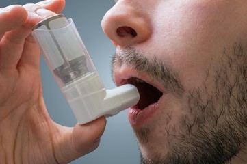 Asthmatic man suffers from asthma and is using inhaler. - obrazy, fototapety, plakaty