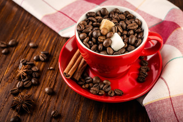Red cup of coffee with coffee beans and sugar cubes on wooden background