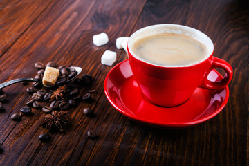 Red cup of coffee with coffee beans and sugar cubes on wooden background