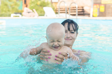 Fototapeta na wymiar Happy baby girl enjoying her first swim in the pool. Mother and daughter on summer vacation. Family values. Parenting and child entertainment. Mom in the decree