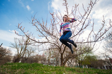 Beautiful happy woman jumping in spring blossoming garden