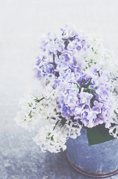 Bouquet of white and purple lilac flowers in metal bowl on grey background