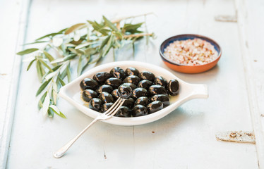Black olives in white ceramic plate, branches and spices over li