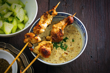 Asian satay chicken skewers on a bowl with sauce, peanut, cucumb