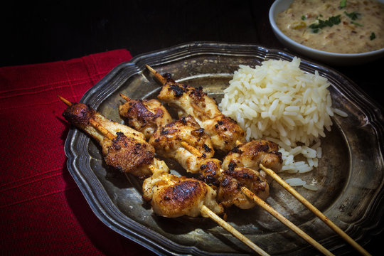 Asian meat skewers with rice and satay peanut sauce on a silver