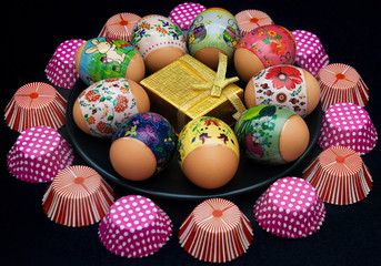 Easter eggs  with beautiful designs and a golden giftbox on black plate surrounded by cupcake holders