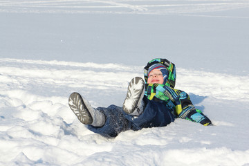 Fototapeta na wymiar The little boy in a color jacket with a hood with a smile lying on snow 