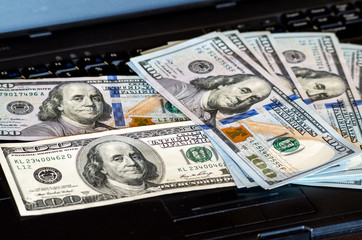 Bunch of dollar bills thrown on a laptop keyboard featured defocused bokeh