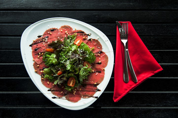 Meat carpaccio on white plate on black wooden background