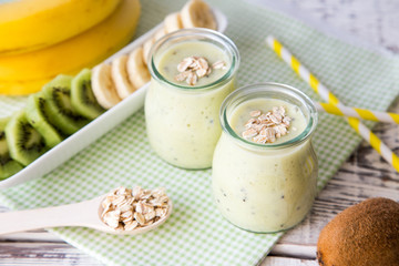 Obraz na płótnie Canvas Banana smoothie with kiwi and oats on a light wooden table. Healthy food