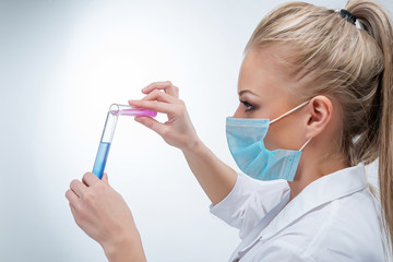 Attractive young blonde female doctor in blue mask with medicine in flasks