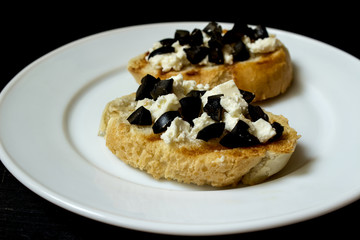 Bruschetta with black olives on a white plate on a black background.