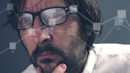 Thinking adult caucasian businessman with beard looking at infographics and charts on computer monitor, eyeglasses with light reflection. - Powered by Adobe