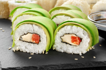 Sushi rolls with avocado, salmon and sesame seeds on slate tray.