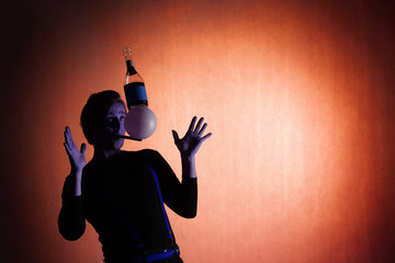 silhouette of a juggler with a balanced bottle and ball in the mouth