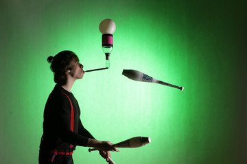 silhouette of a juggler with sticks on a green background - obrazy, fototapety, plakaty