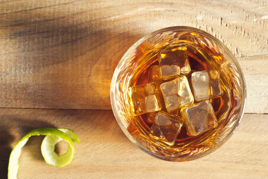 Glass of whiskey with ice on wooden background, top view