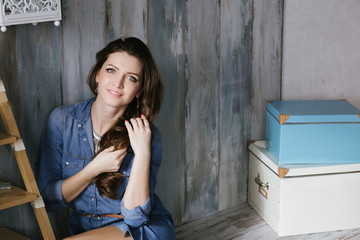 Beautiful woman dressed in denim dress sitting near the bookcase two boxes