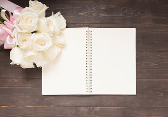White roses flower with ribbon are on the notebook